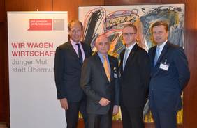 Four men standing in front of a roll-up banner and looking into the camera